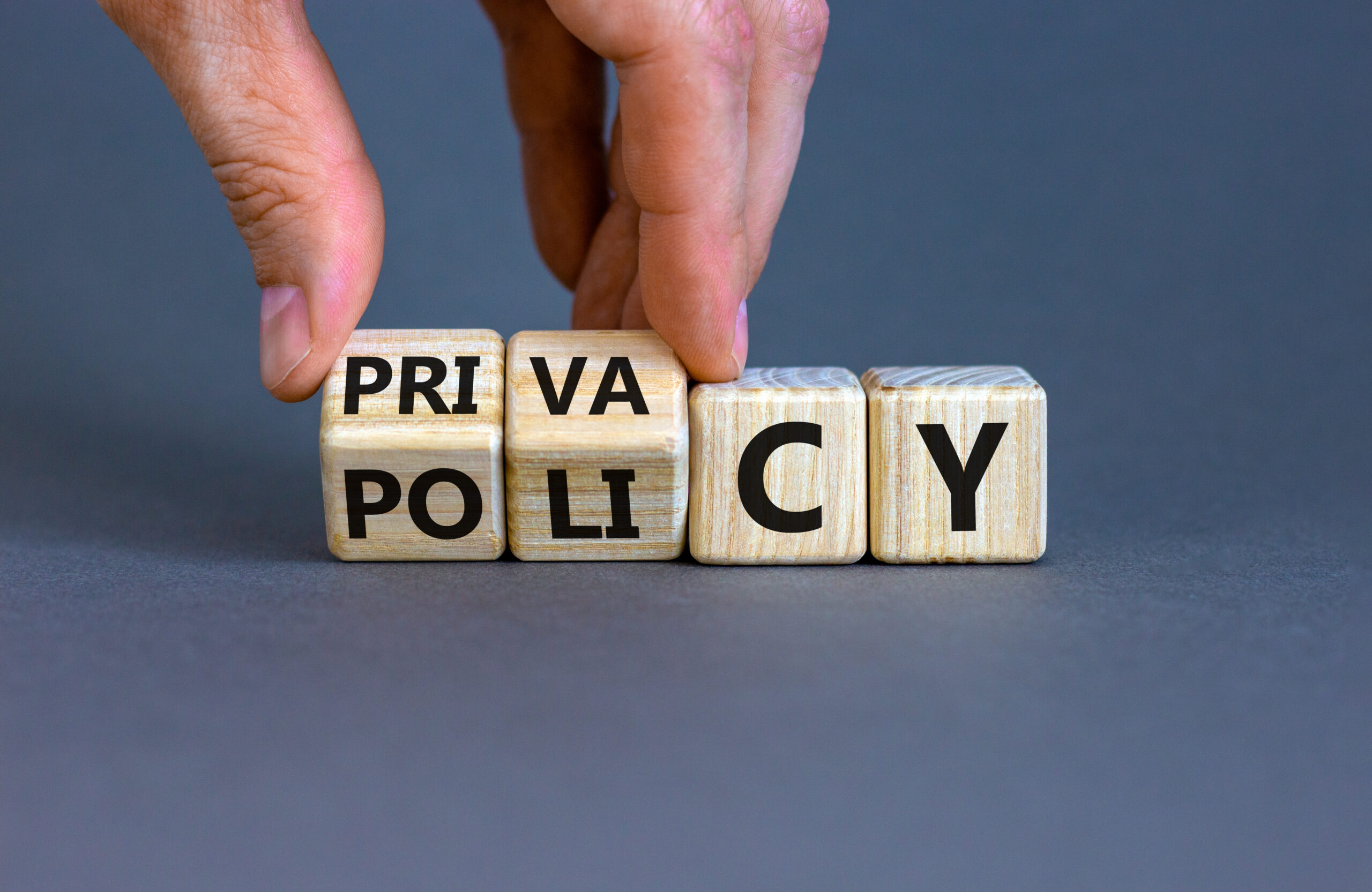 Privacy policy symbol. Hand turns the wooden cube with words ‘Privacy policy’ on a beautiful grey background. Business and privacy policy concept. Copy space.